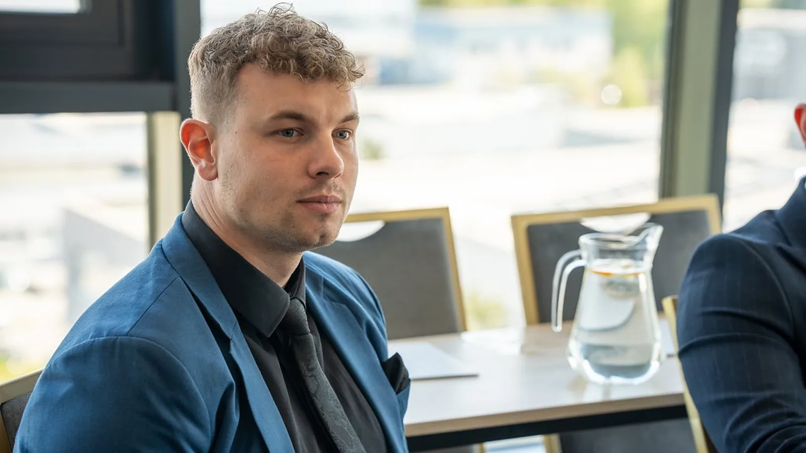 Július Koys v modrom saku pri stole